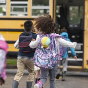Des enfants courent vers un autobus scolaire jaune.