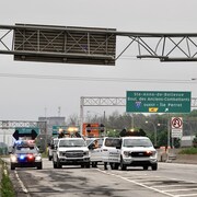 Des camions et une voiture de police sont les seuls véhicules sur l'autoroute. On aperçoit la structure, dont une partie est rompue.