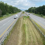 Une camionnette et sa remorque sont stationnées sur la partie gauche de l'autoroute, tandis que des autos circulent sur l'autre partie, en direction est.