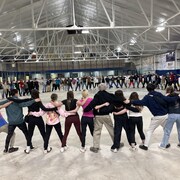 Une centaine de jeunes forment un cercle en s'entrelaçant dans un aréna sans glace. 