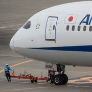 Un membre de l'équipe au sol se trouve sur le tarmac à côté d'un avion de passagers de la compagnie japonaise All Nippon Airways (ANA) à l'aéroport international de Tokyo (Haneda), le 2 février 2023.