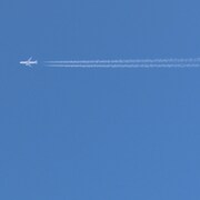 Un avion de ligne vole au loin dans un ciel complètement bleu. Il laisse derrière lui deux traînées blanches.