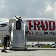 Justin Trudeau salue de la main du haut de la rampe d'accès menant à l'avion du Parti libéral du Canada.