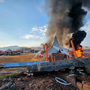 Des flammes jaillissent des restes d'un avion écrasé au sol.