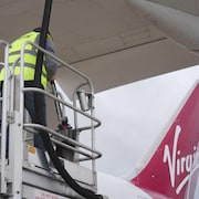 Un employé s'affaire à alimenter un avion de la compagnie Virgin en carburant.
