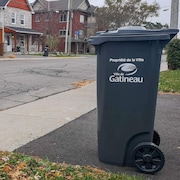 Un bac gris placé près du trottoir, près pour la collecte des ordures