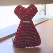 Une épinglette faite en perles rouges et en forme de robe.