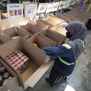 Une femme voilée met de la nourriture dans des boîtes de carton dans une banque alimentaire.