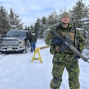 Un militaire avec une mitraillette dans les mains bloque le passage sur une route en forêt en hiver.