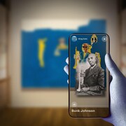 Un dessin montre une main tenant un téléphone intelligent sur lequel s'affiche une image en noir et blanc d'un trompettiste en veston cravate, avec une toile bleue accrochée à un mur en arrière-plan. 