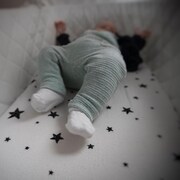 Un bébé couché sur le dos dans son lit, dont on voit les jambes en gros plan.