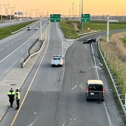 Deux policiers discutent sur une bretelle d'autoroute bloquée par un véhicule renversé.