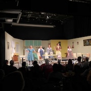 Cinq comédiennes debout sur scène devant un public.