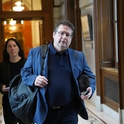 Bernard Drainville marche dans un corridor de l'Assemblée nationale en compagnie d'une attachée politique.