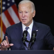Joe Biden, derrière un micro, regarde devant lui.