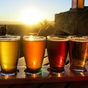 Quatre verres de bière en palette de dégustation sur fond de coucher de soleil.