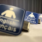 Une photo de trois petites attaches indiquant que l'on peut recevoir un service soit en anglais ou en français. 