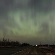 Une route avec au-dessus des aurores boréales dans un ciel étoilé.