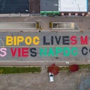 Sur le sol d'une route asphaltée, on peut lire en caractère majuscule multicolore : Bipoc lives matter, les vies napdc comptent.