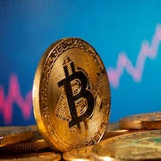 Une pièce illustrant un bitcoin devant un graphique boursier. 