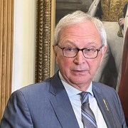 Blaine Higgs répond aux questions des médias, debout devant un grand tableau dans l'édifice de l'Assemblée législative.