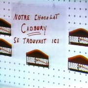 Étagère vide avec des autocollants de la campagne « On barre Cadvury » et une enseigne indiquant « Notre chocolat Cadbury se trouvait ici ».