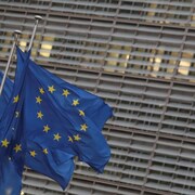 Trois drapeaux de l'Union européenne flottent devant un bâtiment.