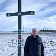 Brian Starkel pose devant la croix verte érigée en mémoire des victimes.