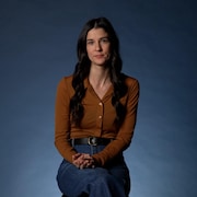 Brigitte est assise dans un studio de Radio-Canada devant un fond bleu uni.