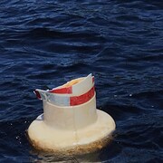 Une balise endommagée flotte sur l'eau d'une rivière. 