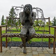 Sculpture de métal représentant une femme à la tête baissée assise sur un banc.