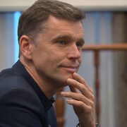 Le maire Marchand sourit en se tenant le menton. 