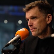 Un homme habillé en noir dans un studio de radio derrière un micro.