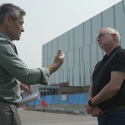 Deux hommes discutent devant un chantier de construction. 
