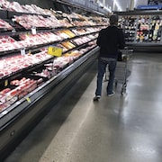 Un homme marche sans s'arrêter devant la section des viandes, à l'épicerie.