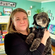 Stacey Button, dans sa maison, tient son petit chien dans ses bras.