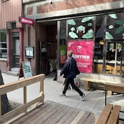 Un piéton marche devant le café éphémère AGATINO, et regarde l'affiche présentant ce dernier.