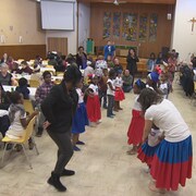 Des enfants et deux animatrices dansent pendant que d’autres personnes assises à leur table les regardent.