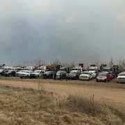 Des camions sont garés devant une route alors que se dégage de la fumée des feux de forêt.