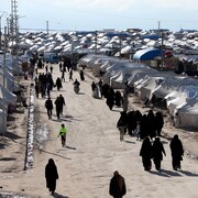 Vue aérienne d'un camp. On voit de nombreuses tentes blanches et des gens, dont des femmes couvertes de la tête au pied, marcher dans une allée. 