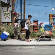 Trois itinérants poussent et tirent leurs affaires sur le trottoir.