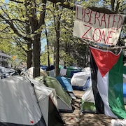 Un campement de manifestants avec un drapeau palestinien et une affiche avec un slogan revendicateur.