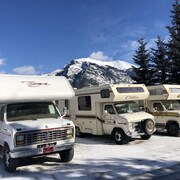 Trois caravanes stationnées les unes à côté des autres. Derrière elles, on voit les Rocheuses. Le ciel est complètement dégagé. C'est l'hiver, on voit de la neige sur le sol.
