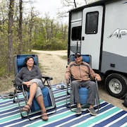 Sandra Lawrence et Gilbert Manitopyes sont assis sur leurs chaises devant leur caravane. 