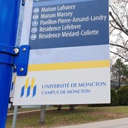 Près d'un sentier, un panneau jaune et bleu indique la direction pour se rendre aux divers pavillons et édifices de l'université.