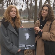 Deux personnes tiennent une pancarte sur laquelle apparaît la photo d'Alexeï Navalny et un message qui annonce un rassemblement pour commémorer son décès.