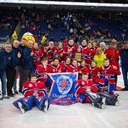 L'équipe pose au centre de la glace avec la bannière et le trophée.