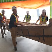 Cinq travailleurs déplacent un canot en bois.