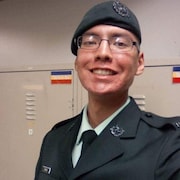 Le caporal Nolan Caribou dans son uniforme militaire et portant un béret sourit devant des casiers.