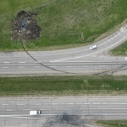 Vue de haut du lieu de l'accident, où un gros trou noir montre là où le véhicule a brûlé.